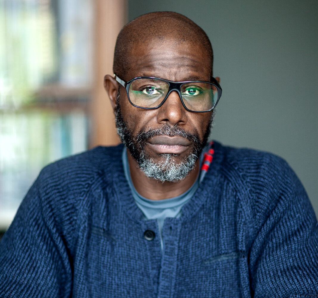 Steve McQueen award winner Erasmus Prize 2026. Steve McQueen dressed in blue with city scape background beyond the window.